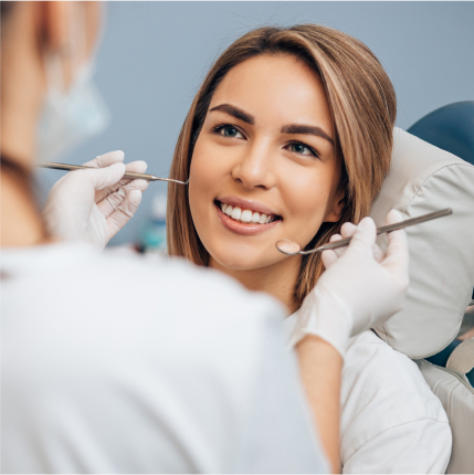 Smiling woman in dental chair during exam with dentist holding instruments near her face.