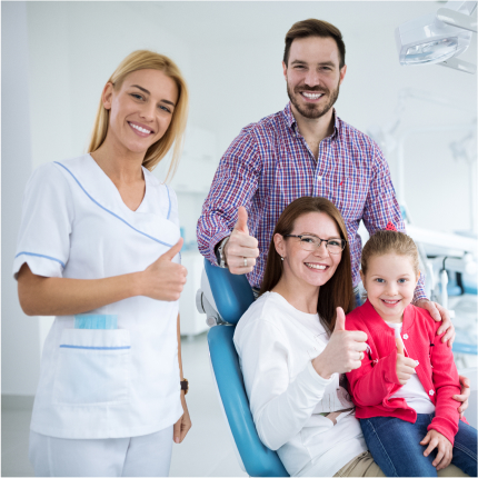 Happy family with young child giving thumbs up at dental office with smiling dental professional.