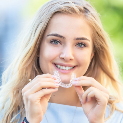a woman smiles while holding a clear aligner