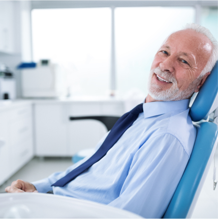 Smiling older man in a dental chair wearing a dress shirt and tie, relaxed after treatment.