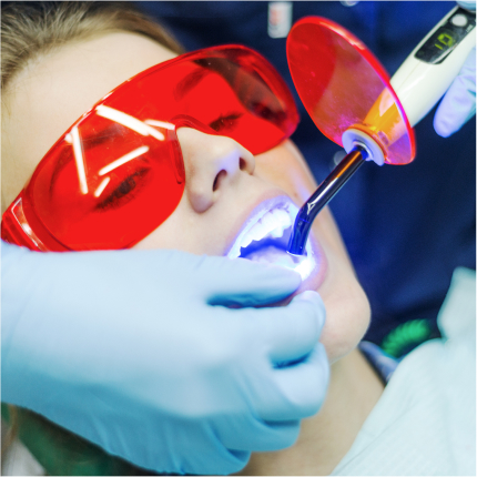 Patient wearing red protective glasses during laser dental treatment with curing light.