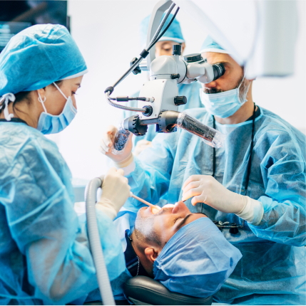 Dental team in surgical attire performing a procedure with a microscope, illustrating advanced gum treatment.