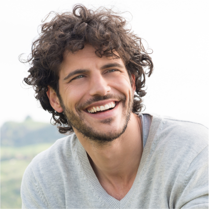 Man with curly hair smiling outdoors, showcasing healthy teeth from dental care.