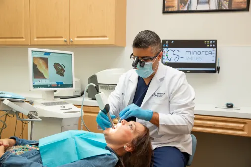 Dentist using digital scanner for CEREC crown procedure on a patient in modern exam room.