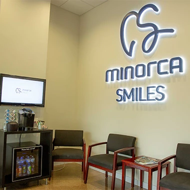 Modern dental office waiting area with Minorca Smiles logo, seating, and refreshment station.