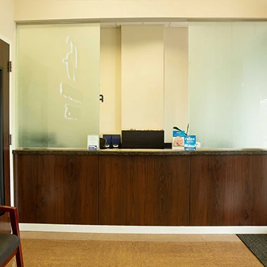 Dental office front desk area with wood paneling, frosted glass, and patient seating.