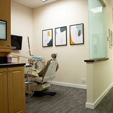 Modern dental exam room with chair, computer, and artwork on wall.