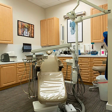 Dental treatment room with beige chair, equipment, and wood cabinetry.